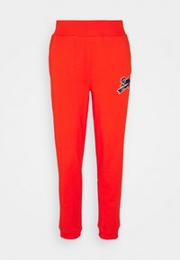 Röda sweatsbyxor av mjuk bomull, med resårmidja och muddar, samt en logotyp i svart på vänster ben.