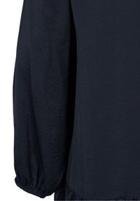 Marinblus i lättviktsmaterial, med långa ärmar och elastiska manschetter samt en volang nertill. Slät textur och flödande design.