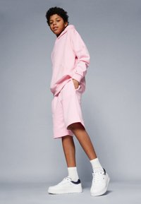 Ljust rosa huva sweatshirt och matchande shorts i mjukt tyg, parat med vita sneakers med mörkblå accenter.