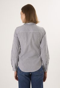 Pruhovaná košile s dlouhými rukávy, šedé a bílé střídající se pruhy, detail na zadním díle, zakřivený lem a zapínání na knoflíky na manžetách.