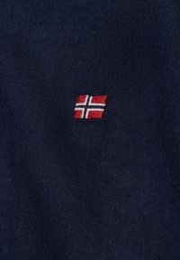 Navy stof met een kleine geborduurde Noorse vlag in rood, wit en blauw, niet in het midden geplaatst, met een gestructureerd oppervlak.