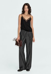 Schwarzes Spaghettiträgertop mit Spitzenbesatz, kombiniert mit hoch taillierten, gestreiften, weiten Hosen. Als Accessoire dient eine kleine, dunkelbraune Handtasche.