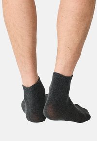 Tummanharmaat nilkkasukat, valmistettu pehmeästä tekstuurimateriaalista, resorilla ja hieman kuluneilla kohdilla pohjissa.