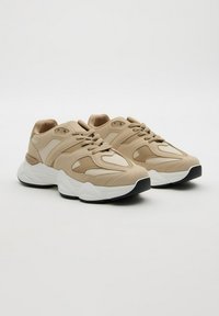 Zapatillas chunky en beige y crema con paneles texturizados, cordones en la parte delantera y suelas gruesas en blanco con acentos de tracción negra.