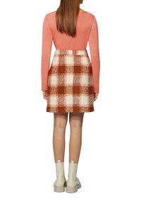 Langsleeve roze top en een aansluitende rok met een geruit patroon in oranje en wit. Dragend met beige enkellaarsjes.