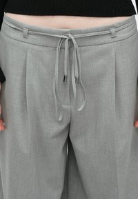 Hallid laiade jalgadega püksid, millel on paelaga vöökoht, sile tekstuur ja metallist detailid paela otstes.