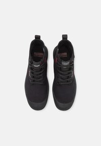 Sneaker alte nere in tela con suole in gomma. Presentano lacci rotondi, un anello sul tallone e dettagli rossi vicino al marchio.
