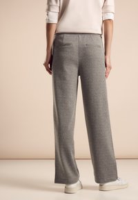 Pantalons larges gris texturés avec taille haute, dotés de poches arrière et d'une ceinture lisse, associés à des sneakers blanches.