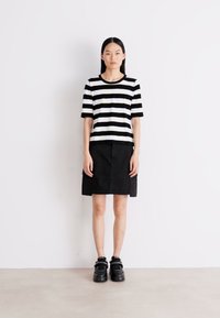 Zwart-wit gestreepte top met korte mouwen, gecombineerd met een zwarte rok en zwarte chunky sneakers. Eenvoudige, strakke lijnen en contrasterende kleuren.