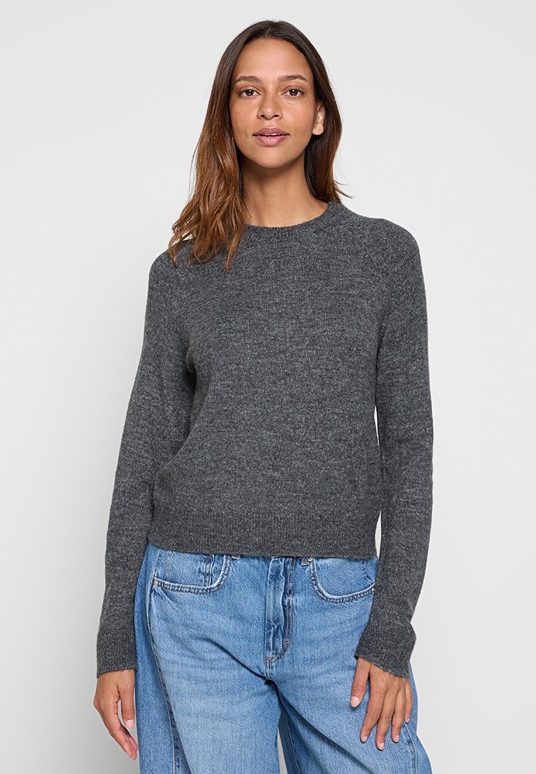 Grijze gebreide trui met lange mouwen, ronde hals en een relaxte pasvorm. Gecombineerd met blauwe high-waisted jeans, wat een casual uitstraling geeft.