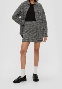 Černo-bíle pruhovaná oversized košile, spárovaná s černým topem a sladěnou sukní, doplněná černými mokasíny a bílými ponožkami.