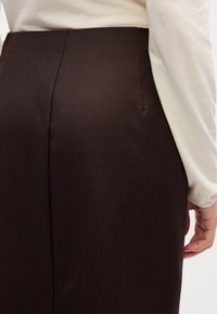 Jupe ajustée marron en tissu texturé, avec une finition lisse et un discret détail de couture à l'arrière.