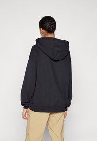 Svart oversized hoodie med en framåtvänd känguruficka. Har en justerbar huva och ribbade ärmslut. Mjuk tygkvalitet och avslappnad silhuett.