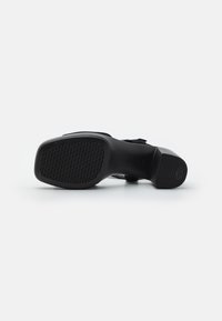Scarpa nera con tacco caratterizzata da una tomaia liscia e una suola in gomma testurizzata con grip a motivi, che presenta una silhouette elegante e un dettaglio con fibbia.
