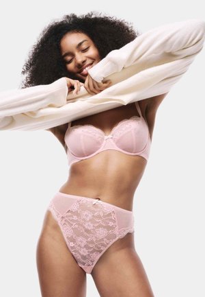 Ensemble de lingerie rose clair comprenant un soutien-gorge en dentelle et une culotte taille haute. Les détails incluent des motifs floraux en dentelle et un accent en satin en forme de nœud.