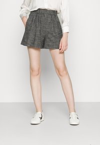 Un short à carreaux gris avec une large taille, des plis et une forme structurée, assorti à des baskets blanches avec des accents noirs.