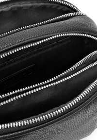 Bolso de cuero negro con tres compartimentos, con cremalleras plateadas y un exterior texturizado. El forro es de tela negra.