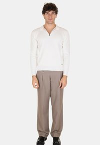 Pullover bianco in maglia leggera con mezza zip, abbinato a pantaloni beige larghi e scarpe nere, creando una palette di colori neutra.