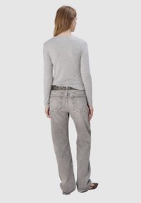 Szary, długi rękaw top zestawiony z jasnoszarymi spodniami o szerokich nogawkach, które mają charakterystyczny design kieszeni oraz znacznikowy czarny pasek.