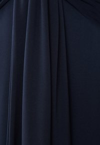 Il tessuto blu navy si adagia elegantemente, caratterizzato da una consistenza morbida e pieghe delicate. Il materiale appare leggero e fluido con una finitura liscia.