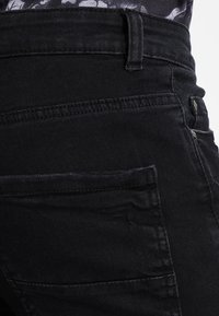 Pantalons en denim noir avec une taille haute, des coutures détaillées et une finition texturée. Comprend des poches latérales et arrière avec des accents en métal.