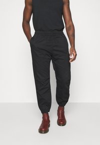 Svarta joggerbyxor med elastisk midja och sidofickor, tillverkade av ett smidigt tyg; kombinerade med vinröda ankelboots.