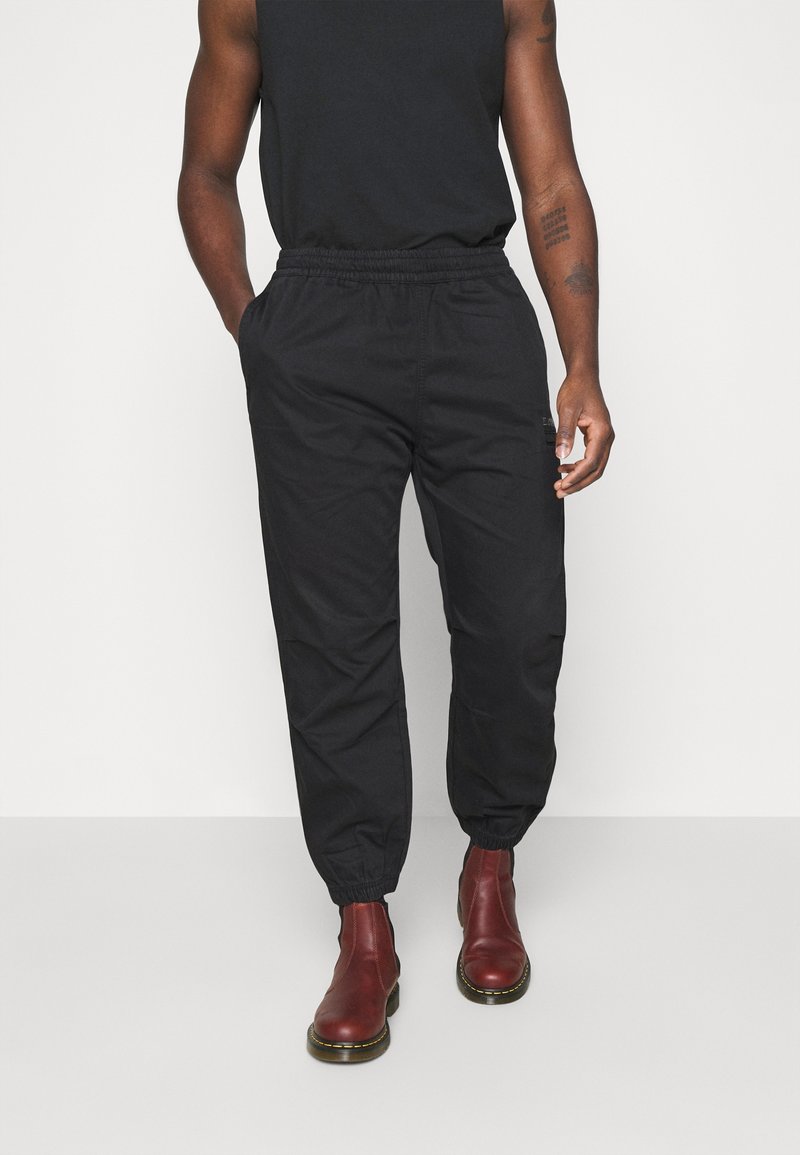 Svarta joggerbyxor med elastisk midja och sidofickor, tillverkade av ett smidigt tyg; kombinerade med vinröda ankelboots.