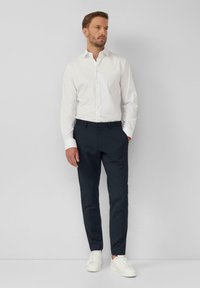 Witte button-up shirt, marineblauwe broek en witte sneakers. Slim fit met een gladde textuur. Eenvoudig ontwerp zonder zichtbare patronen of accenten.