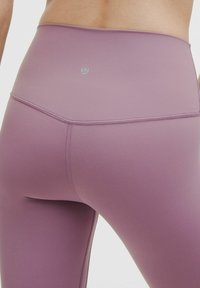 Legginsy w kolorze lawendowym z wysokim stanem, wykonane z gładkiego, elastycznego materiału, z subtelnym logo i płaskimi szwami dla komfortu i wsparcia.