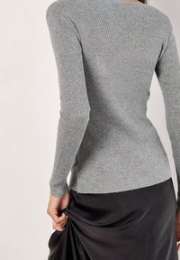 Harmaa ribbineulottu pitkähihainen paita, jossa istuva malli. Pehmeä pinta, kevyt hohto ja sivuhalkiot, yhdistetty liehuvaan mustaan hameeseen.