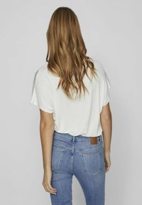 Top bianco a maniche corte con una vestibilità rilassata, abbinato a jeans in denim azzurro chiaro con tasche posteriori e un'etichetta in pelle sulla cintura.