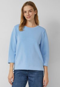 Jasnoniebieska bluza z okrągłym dekoltem, rękawami do łokcia i gładką fakturą. W połączeniu z ciemnymi jeansami. Prosty i swobodny design.