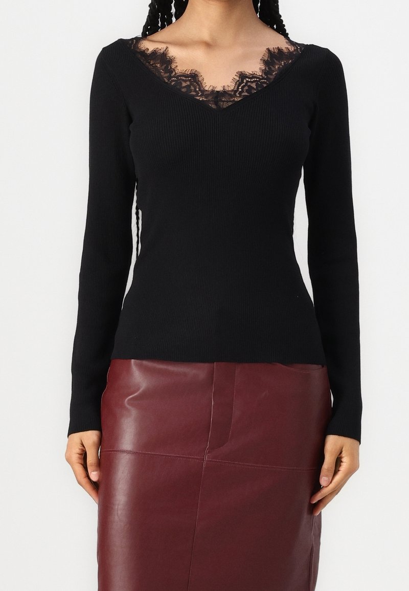 Femme portant un haut noir à manches longues avec un détail en dentelle au niveau du col et une jupe en cuir bordeaux taille haute.