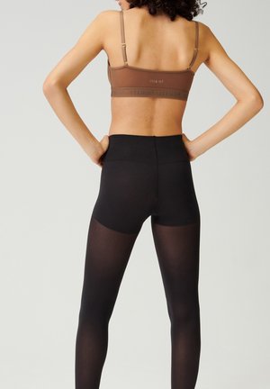 Bruine sportbeha met een gestructureerde band, gecombineerd met zwarte tights met een gladde afwerking en een hoge tailleband. Achteraanzicht weergegeven.