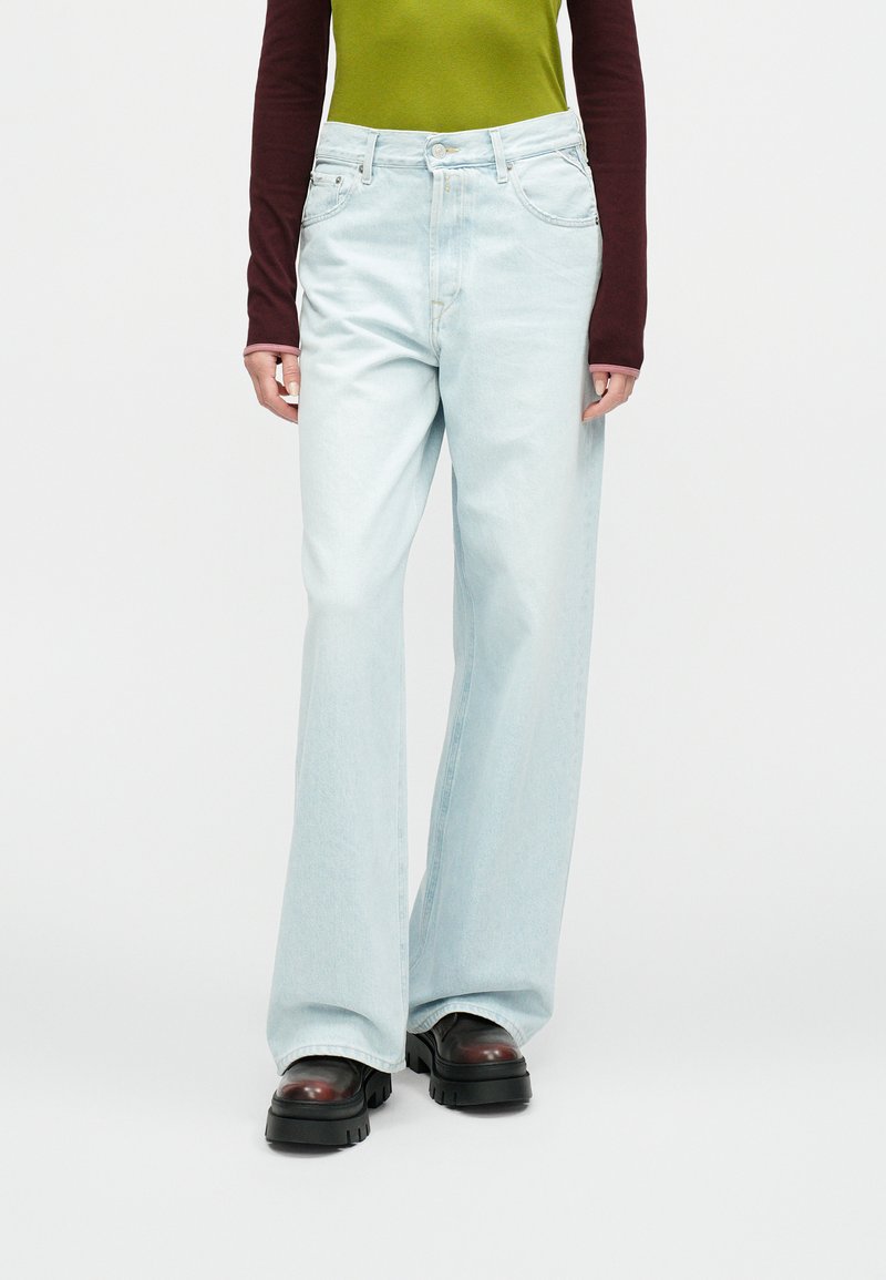 Ανοιχτό μπλε τζιν παντελόνι με φαρδιά μπατζάκια και ψηλή μέση, με απαλή υφή ντένιμ, συνδυασμένο με πράσινο και βαθυκόκκινο μακρυμάνικο τοπ και χοντρά μαύρα παπούτσια.