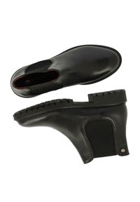 Botas de cuero negras hasta el tobillo con paneles laterales elásticos, suela de goma texturizada y un acabado suave. Costuras notables a lo largo del borde.