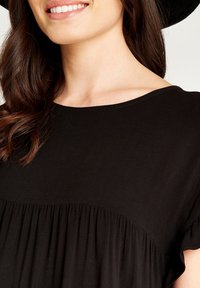Schwarzes Kurzarmtop mit rundem Ausschnitt und gerafftem Stoff an der Taille, das aus glattem Material und subtilen Nähdetails besteht.