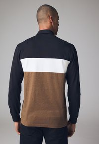 Långärmad polo tröja med svart övre del, vit horisontell rand och brun nedre del. Slät tyg med kontrasterande färger.