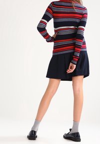 Suéter de punto a rayas en rojo, azul marino y blanco; combinado con una falda azul marino. Calcetines grises y zapatos negros completan el atuendo.