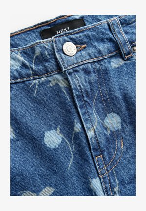 Heledan sinine denimkangas, millel on lilleline muster. Sisaldab hõbedast nööbikinnitust ja pruuni õmblust servadel. Brändi silt on nähtav.