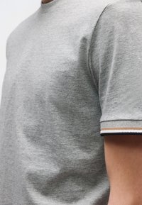 Szürke környakas rövid ujjú póló, kontrasztos csíkozású mandzsettákkal. Puha tapintású és kényelmes szabású.