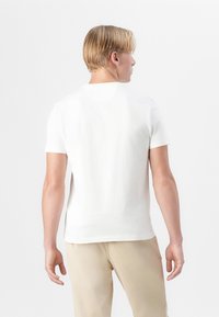 Bílé tričko s krátkým rukávem vyrobené z měkké látky, s kulatým výstřihem, slim fit střih a hladkou texturou, zobrazené ze zadní strany.