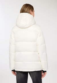 Giacca imbottita bianca con cappuccio, caratterizzata da un design trapuntato e una texture liscia. La giacca ha un taglio dritto e polsini elastici.