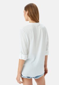 Witte langemouwen shirt gemaakt van lichtgewicht stof, met opgerolde mouwen en een kraagontwerp, gezien vanaf de achterkant.