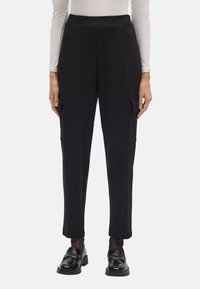 Pantalones cargo negros con un diseño ajustado, fabricados en un material suave. Las características incluyen bolsillos laterales y dobladillos ajustados, combinados con zapatos brillantes.