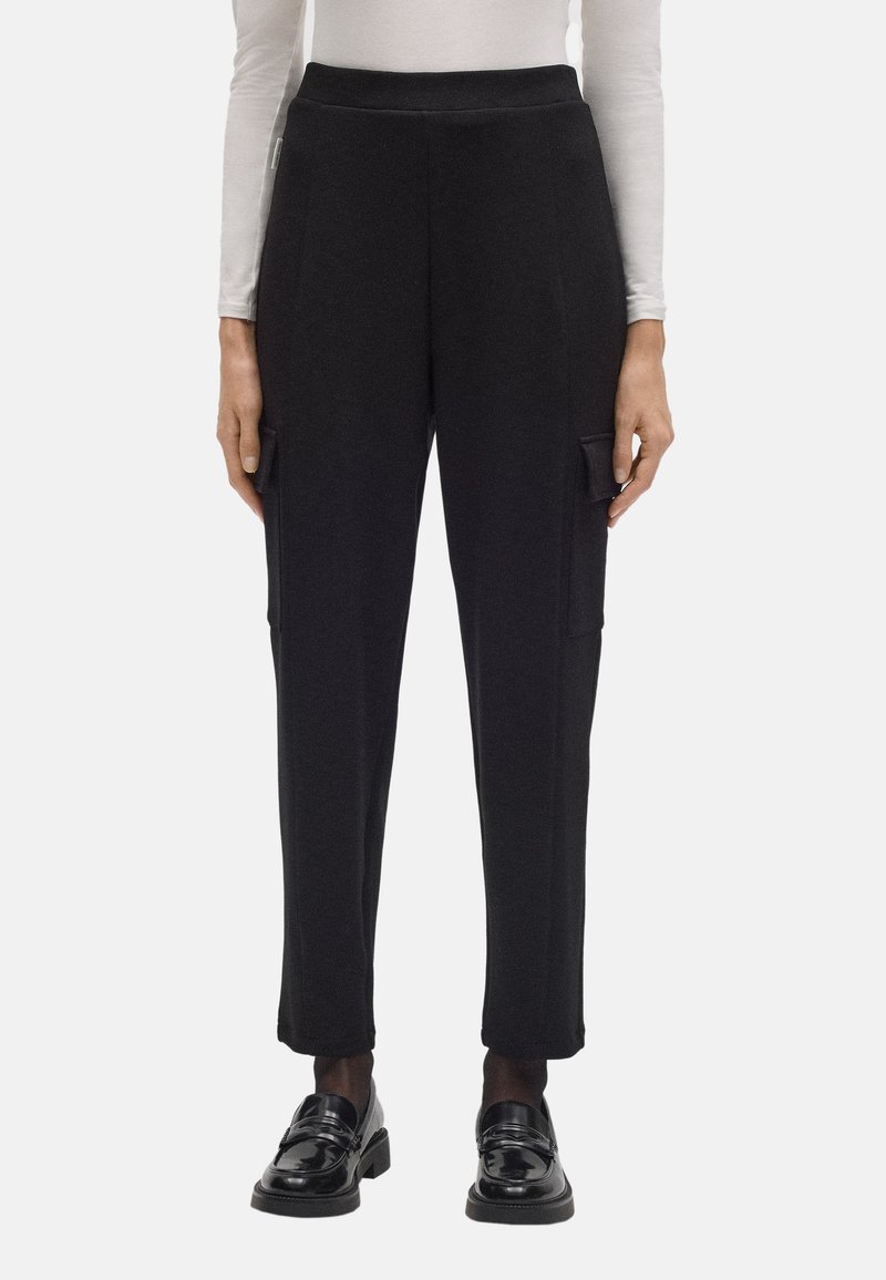 Pantalones cargo negros con un diseño ajustado, fabricados en un material suave. Las características incluyen bolsillos laterales y dobladillos ajustados, combinados con zapatos brillantes.