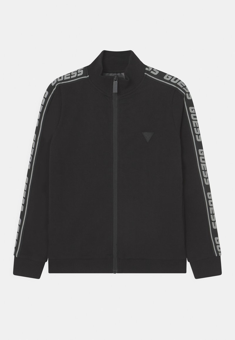 Veste noire zippée avec col haut, bande "GUESS" de marque sur les manches, et petit logo triangulaire sur le côté gauche de la poitrine.