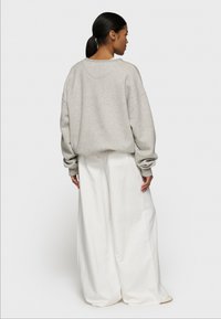 Overdimensioneret grå sweatshirt med sænkede skuldre, ribbet kant og brede cremebukser med en glat tekstur, fotograferet bagfra.