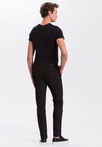 Czarny t-shirt z krótkim rękawem w połączeniu z ciemnymi, dopasowanymi spodniami w kratę i czarnymi butami. Zauważalne detale to dopasowany krój i gładkie tekstury.