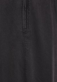 Close-up van zwart denimstof met een verticale naad en deels zichtbare zak met gedetailleerde stiksels.